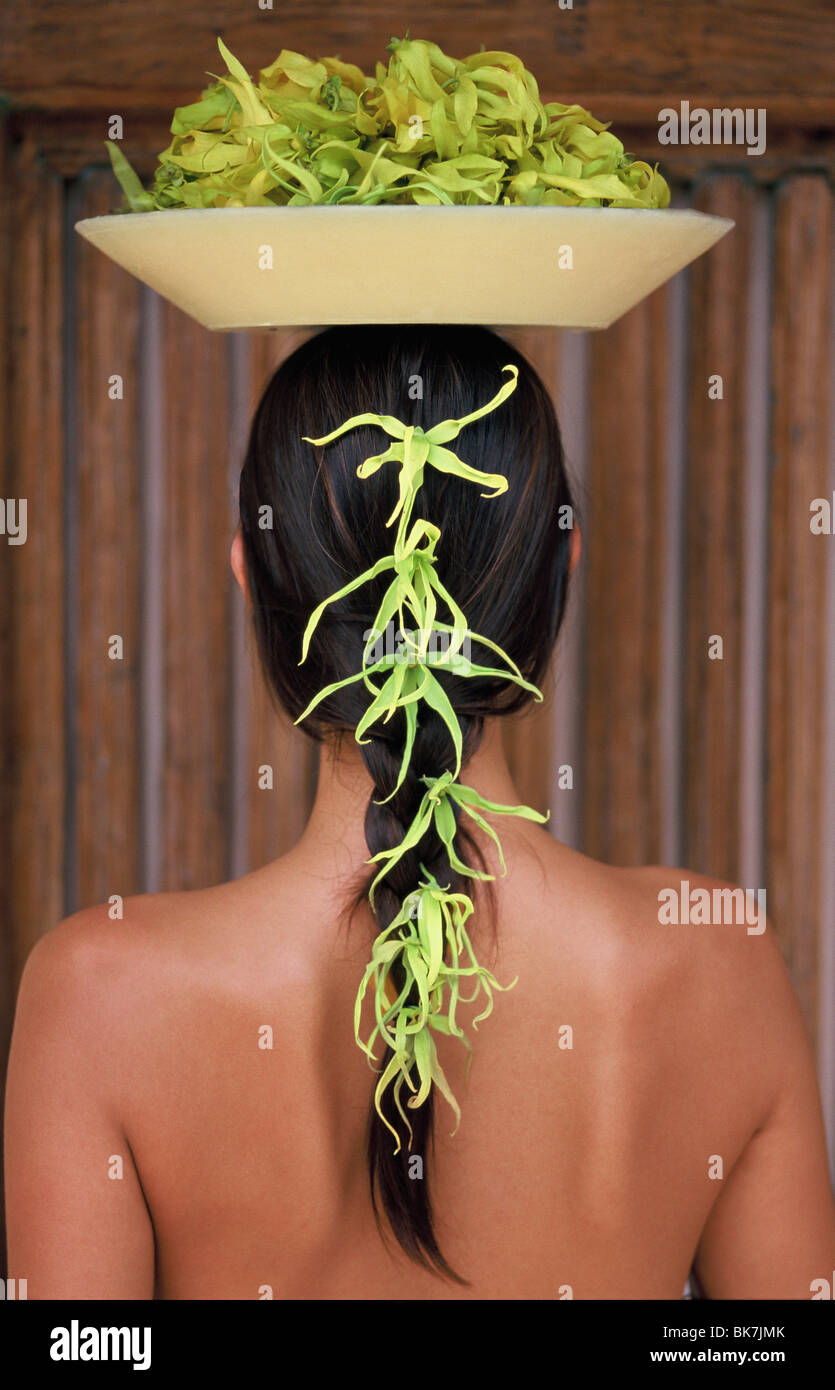 Back view of young woman with long hair balancing a bowl of ylang ylang on her head Stock Photo