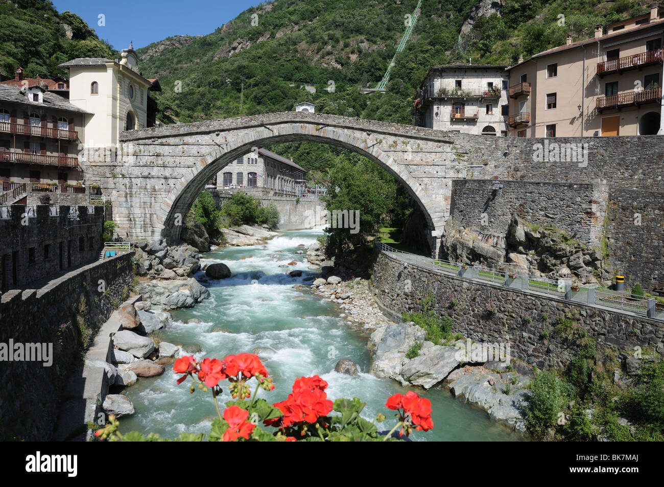 Roman bridge over torrente Lys Pont St Martin Aosta Valley Italy Hydro electric generator can be seen under bridge with Chapel Stock Photo
