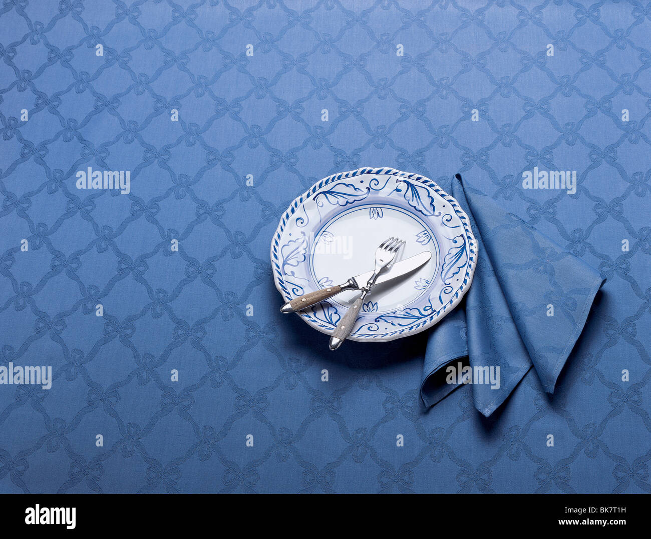 Blue plate on blue brocaide table cloth with knife and fork. Stock Photo