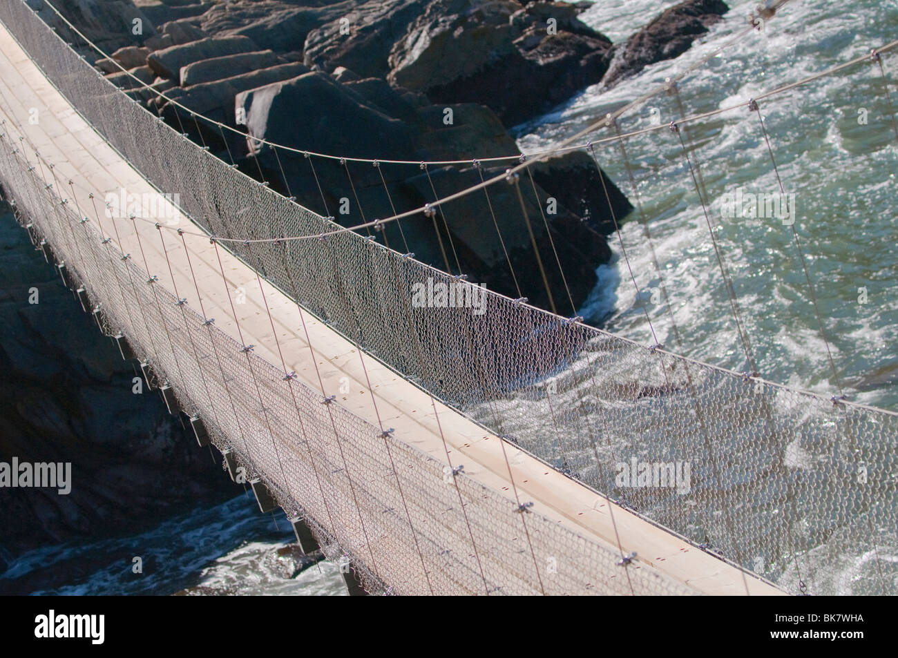 Suspension bridge for trekker over a raging river mouth Stock Photo