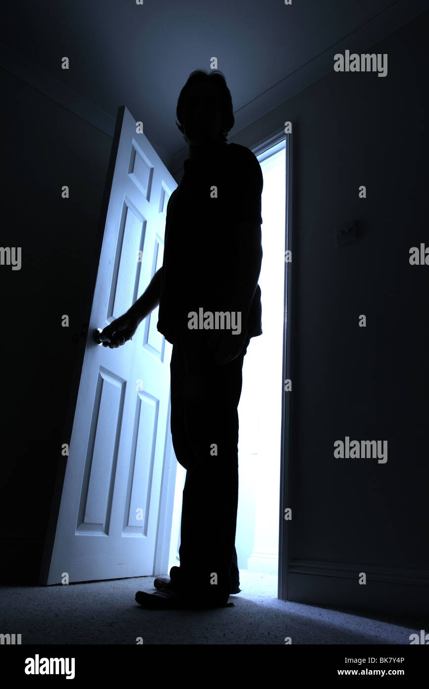 Silhouette of a male entering a dark room with a shaft of light behind Stock Photo