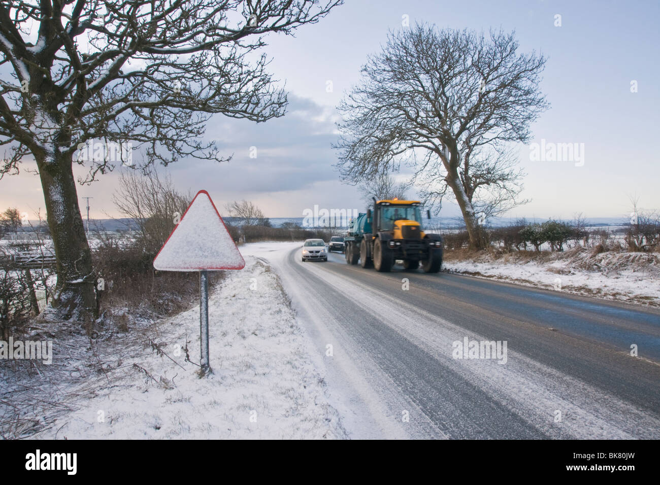 Road warning sign covered with snow alongside a slush covered road, North Yorkshire, UK Stock Photo