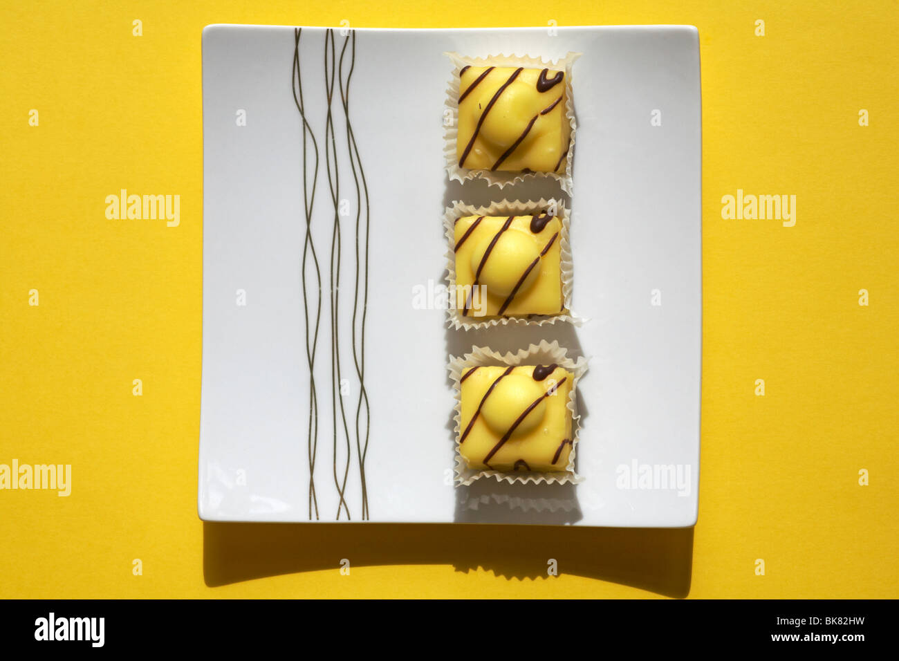 Three Special Edition Lemon French Fancies by Mr Kipling on white plate set on yellow background Stock Photo