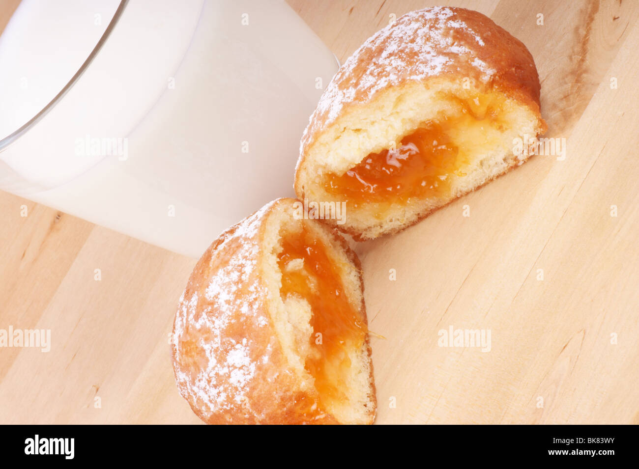 A cup of milk and a freshly made Berliner with apricot jam and powdered sugar. Studio shot. Stock Photo