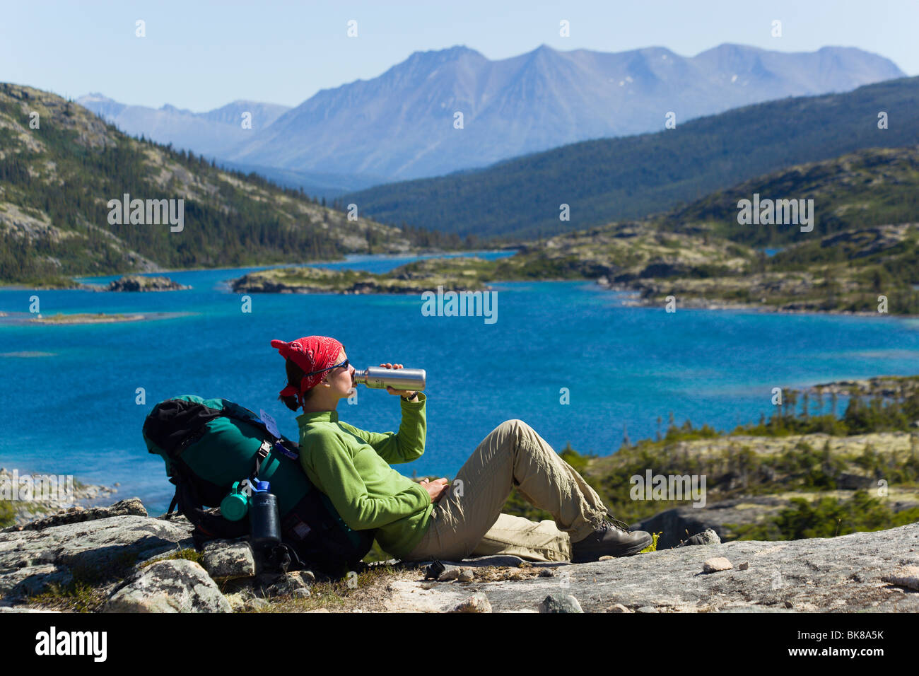 Young woman, hiker, backpacker, sitting on a rock, drinking, resting, enjoying panorama, Deep Lake, historic Chilkoot Pass, Chi Stock Photo