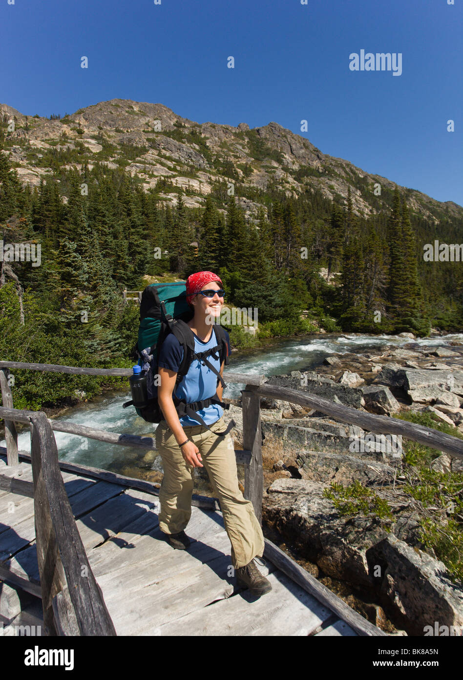Young woman hiking, backpacking, crossing a wooden bridge, hiker with backpack, historic Chilkoot Pass, Chilkoot Trail, near De Stock Photo