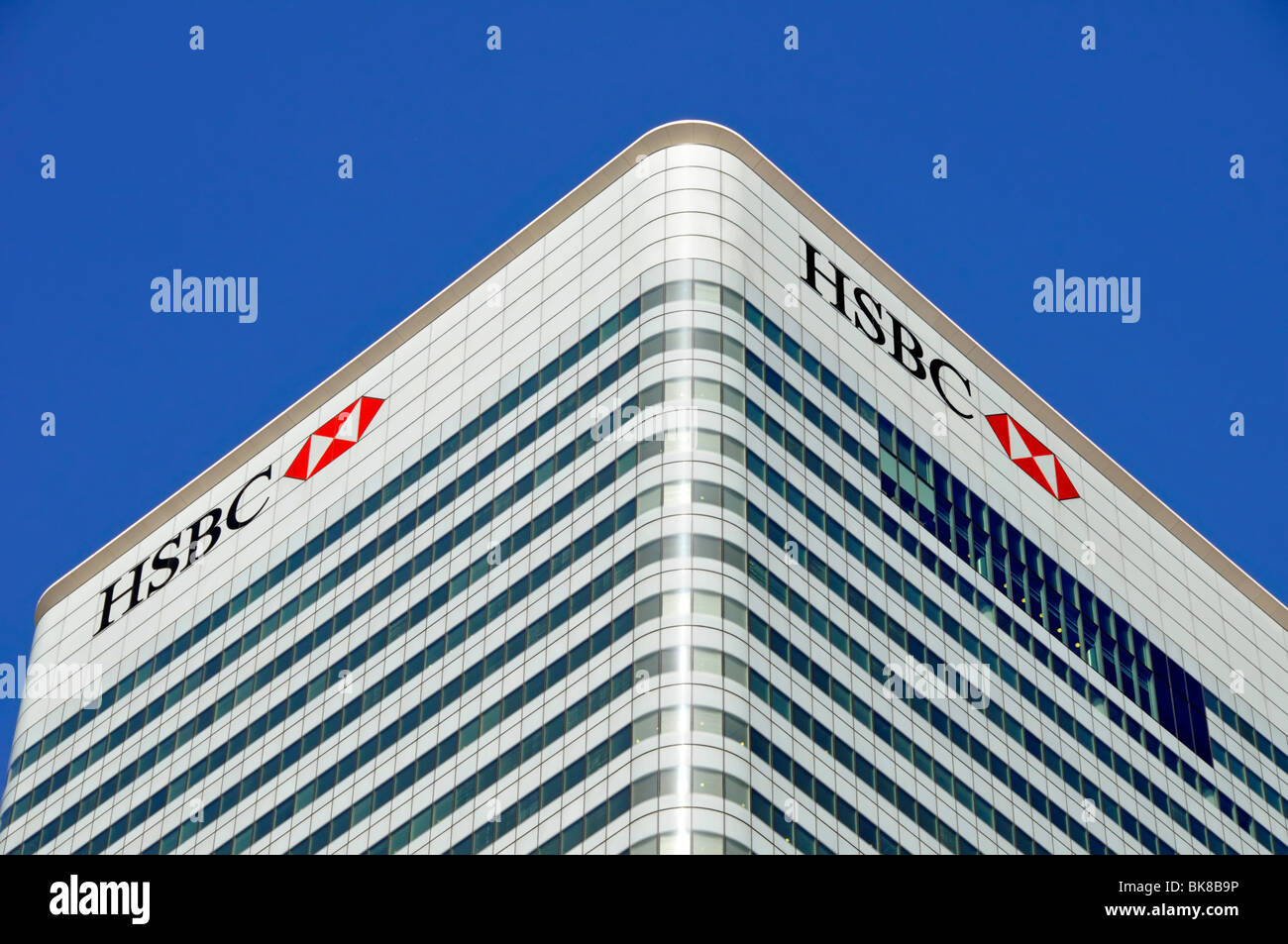 Docklands blue sky corner view of cladding & windows to roof level HSBC bank logo signs at London Docklands Canary Wharf HQ building Tower Hamlets UK Stock Photo