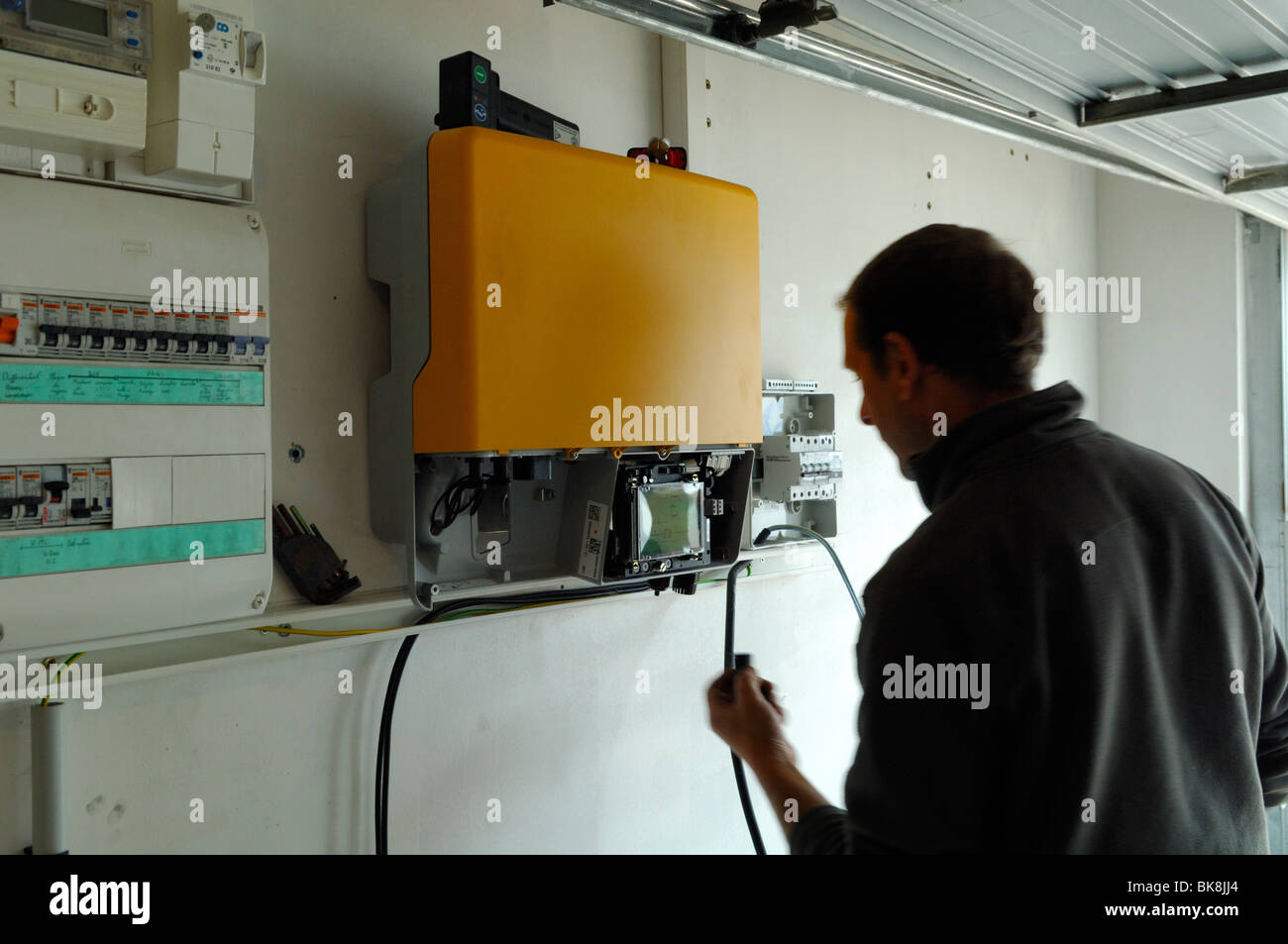 Installation by a technician of a grid tied inverter to converte DC voltage from photo-voltaic solar panels in AC. France Stock Photo