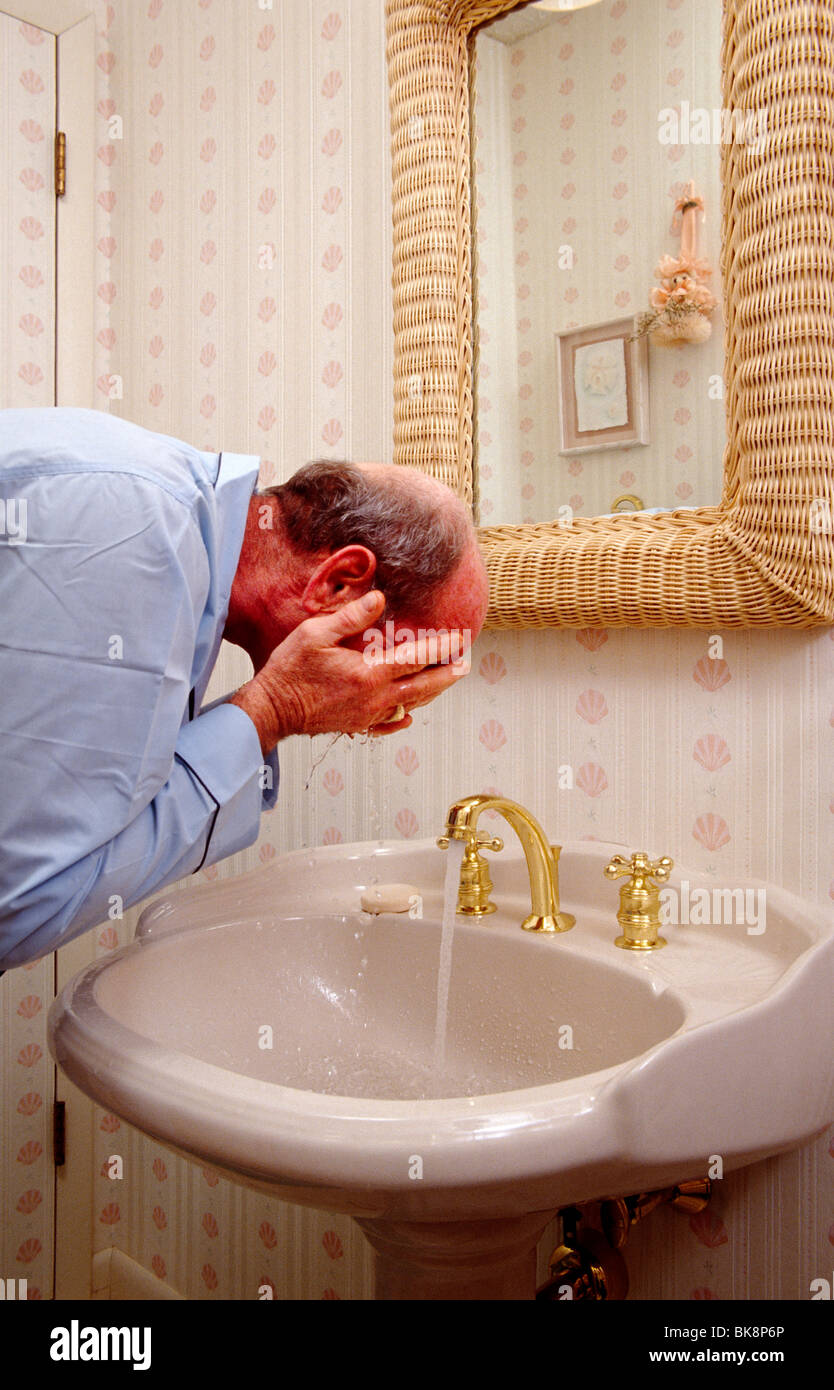 Elderly man in his pyjamas washing his face in his bathroom. Stock Photo