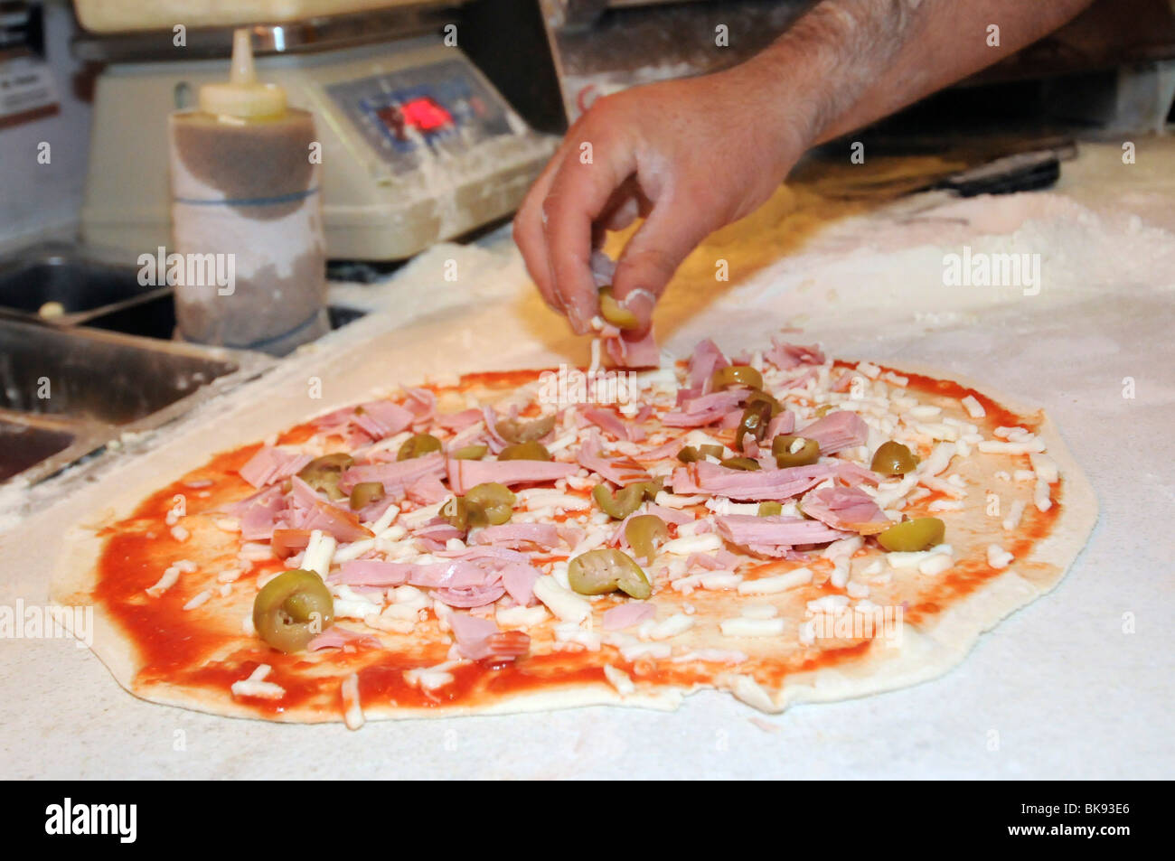Stages of pizza preparation adding olive and ham toppings Stock Photo