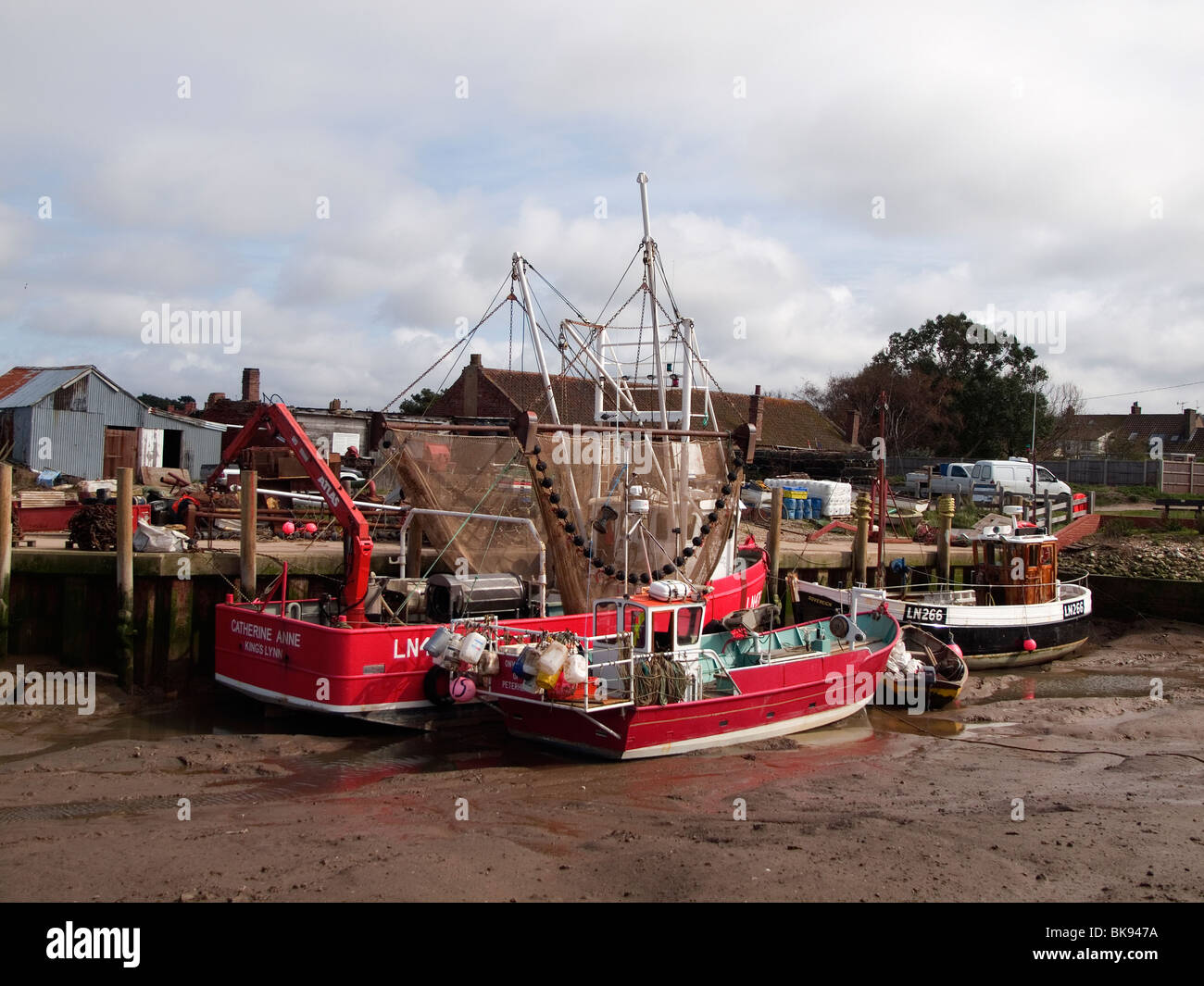 Fishing boats one with hanging beam trawl nets in the harbour at Brancaster North Norfolk Stock Photo