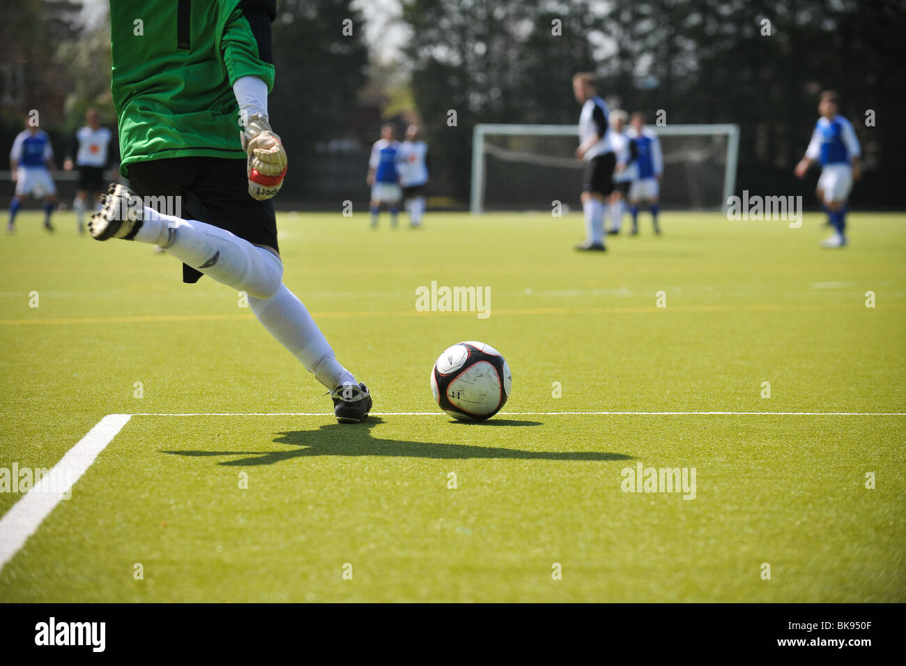 A Goalkeeper clears a football up field during a English amateur Football/Soccer game as the sun beats down. Stock Photo