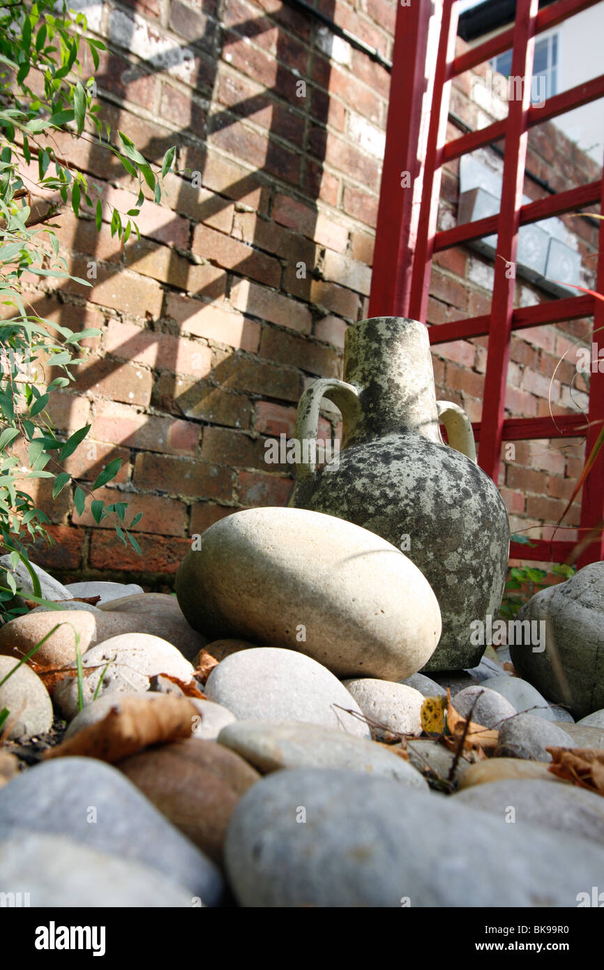 Decorative urns and pots alongside stones and a red fence in a garden setting, with a Victorian built brick wall as a backdrop Stock Photo