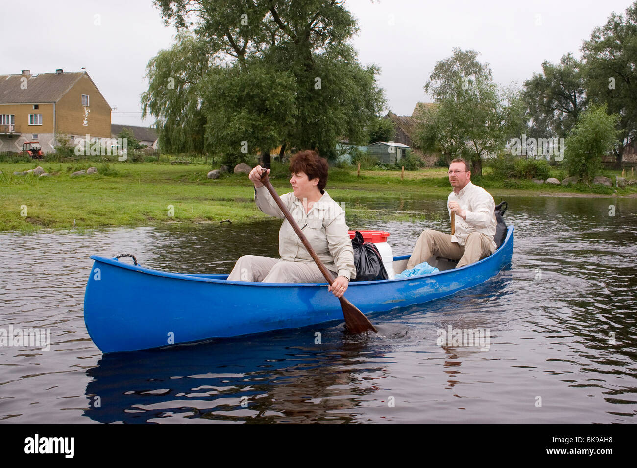 Woman and man paddling their blue canoe along a shore with houses and