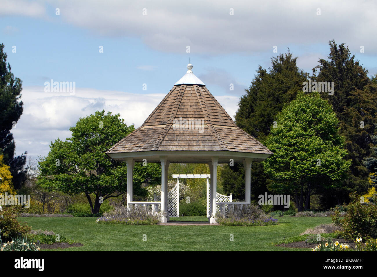 A garden gazebo in early spring framed with green trees a blue sky and