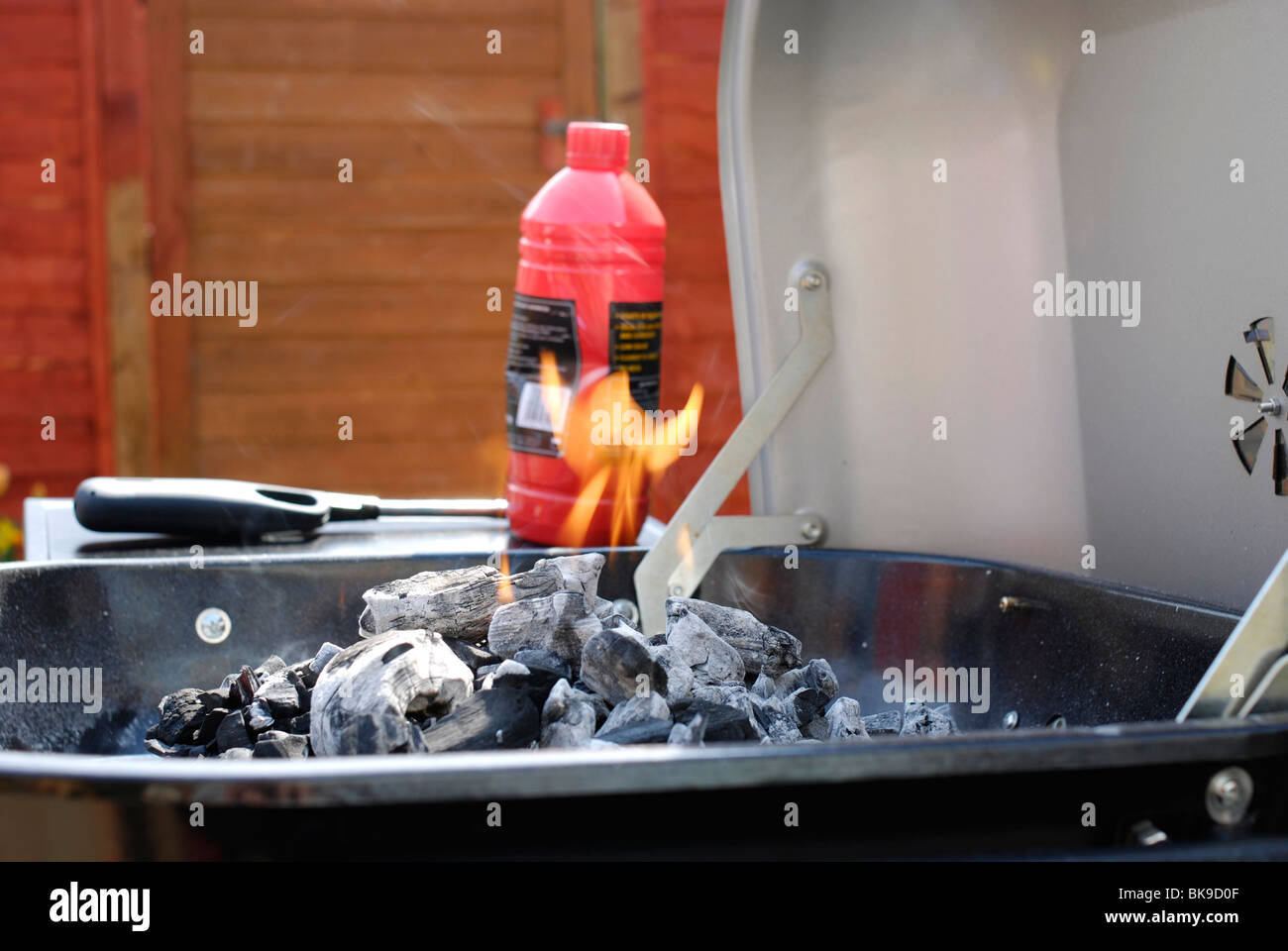 Charcoal barbeque with flame burning in front of bottle of lighter fuel