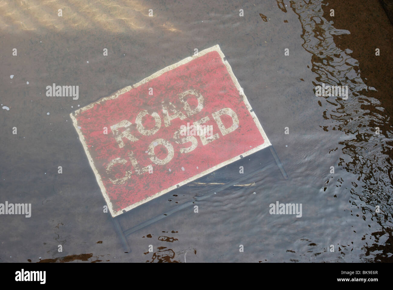 Road closed sign submerged under water. Flooding causing infrastructure and transport problems. Stock Photo
