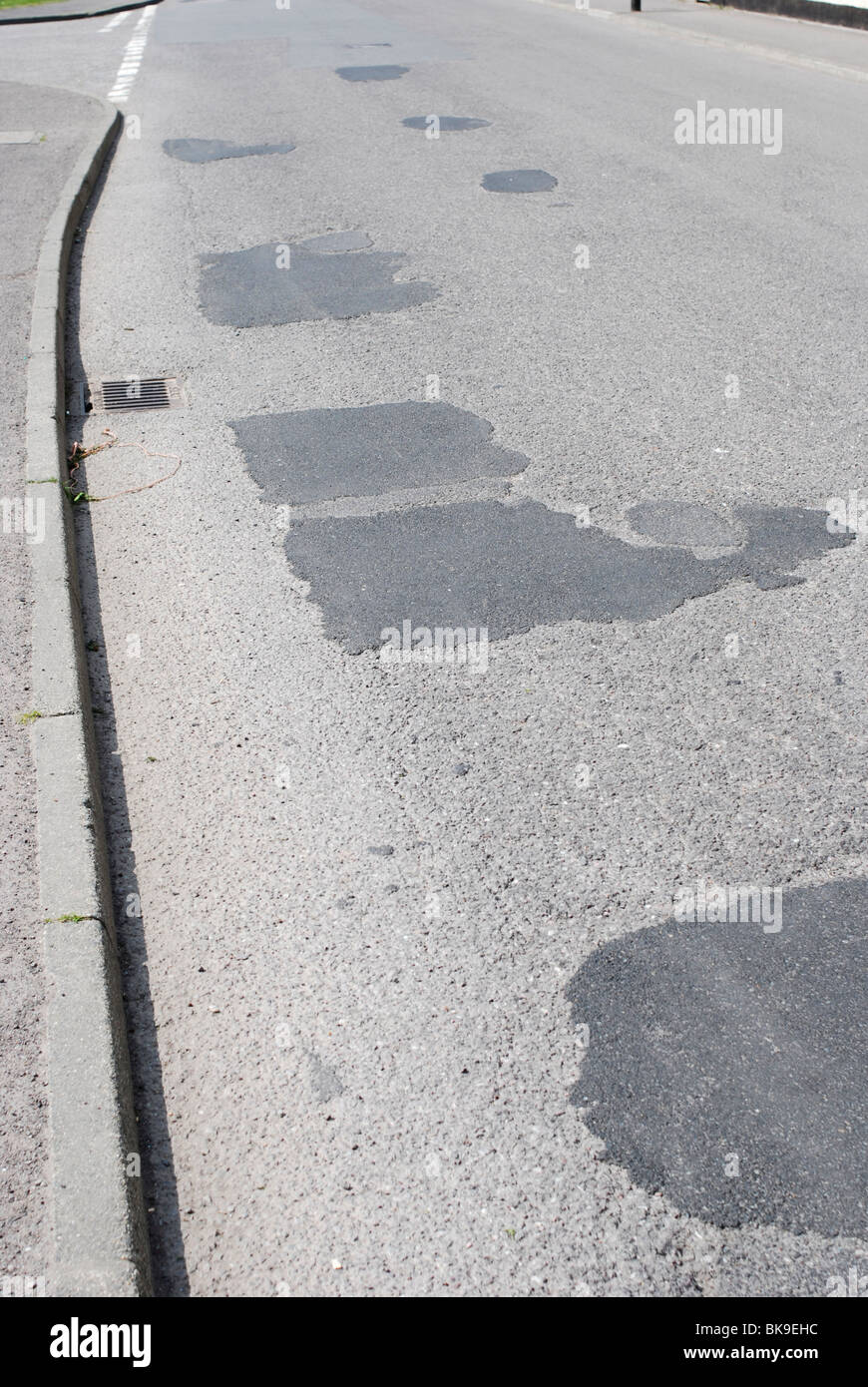 Patchwork repairs on a damaged road surface. Stock Photo
