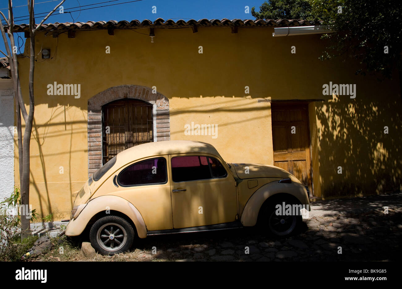 Orange Volkswagen Beetle car parked outside an orange painted colonial house, Suchitoto, El Salvador Stock Photo