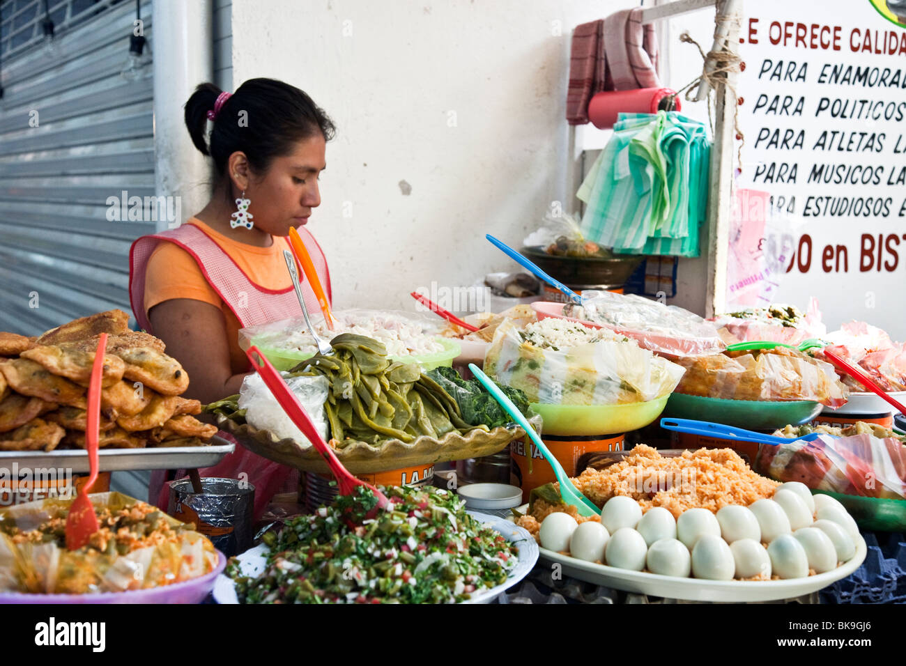 young woman with teddy bear earring selling a tempting array of deli type prepared foods in Benito Juarez market Oaxaca Mexico Stock Photo