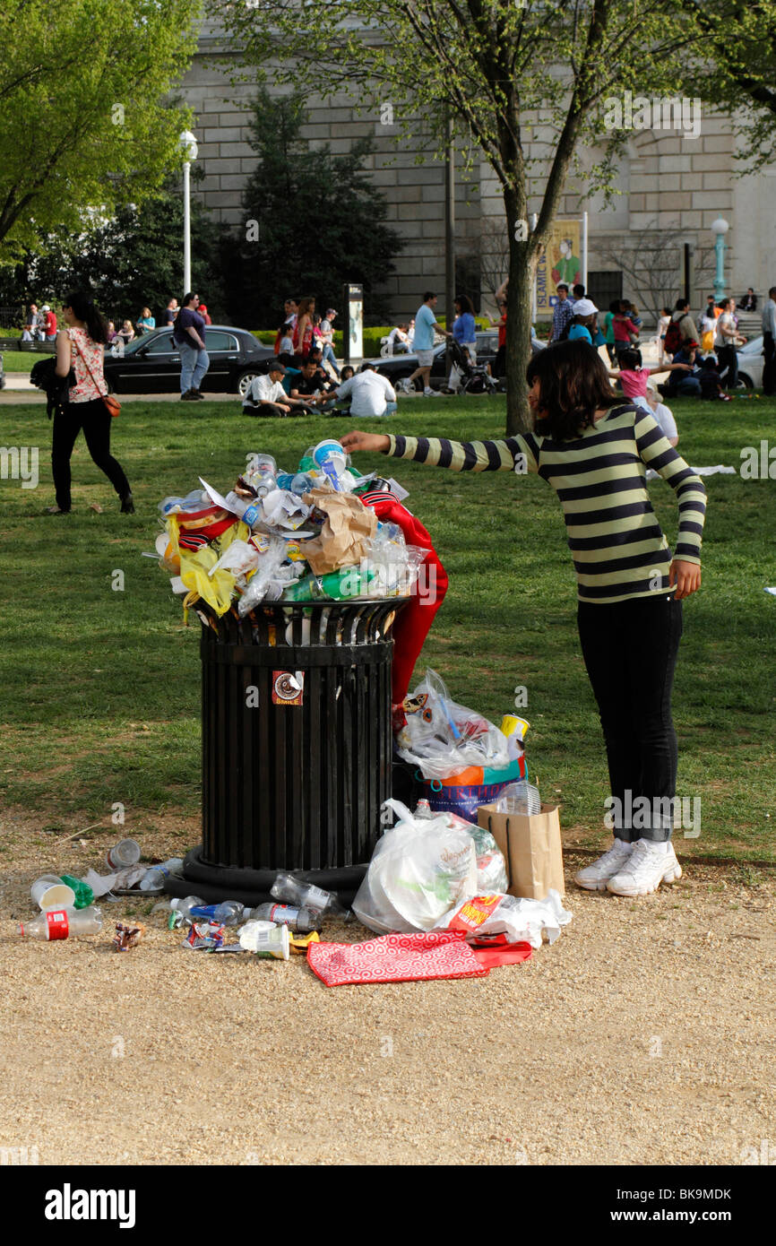 Young girl places garbage in an overflowing bin Stock Photo
