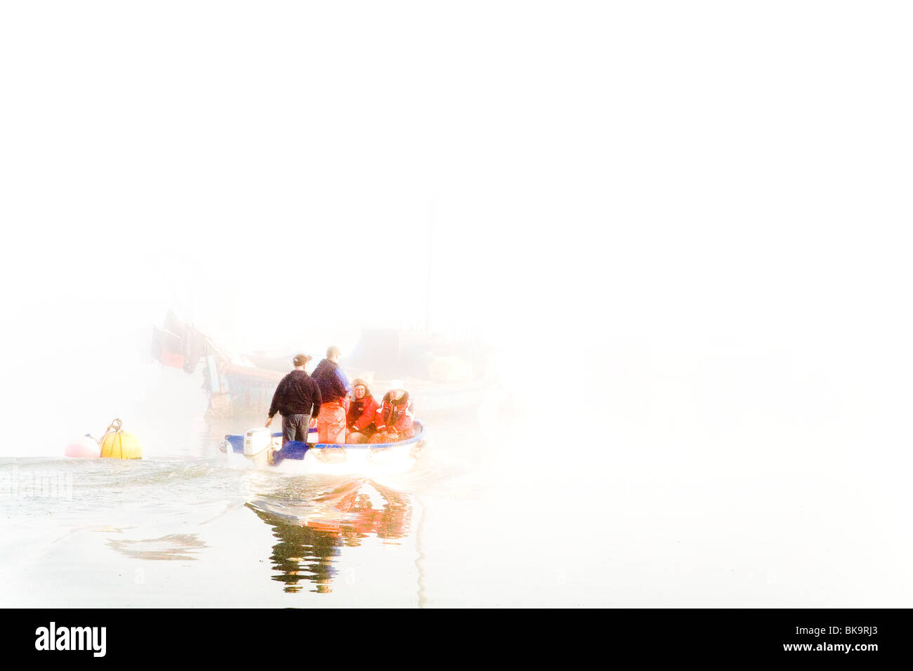 A SMALL BOAT WITH FISHERMEN, HEADS OUT TO THEIR LARGER BOAT IN THE  EARLY MORNING MIST Stock Photo