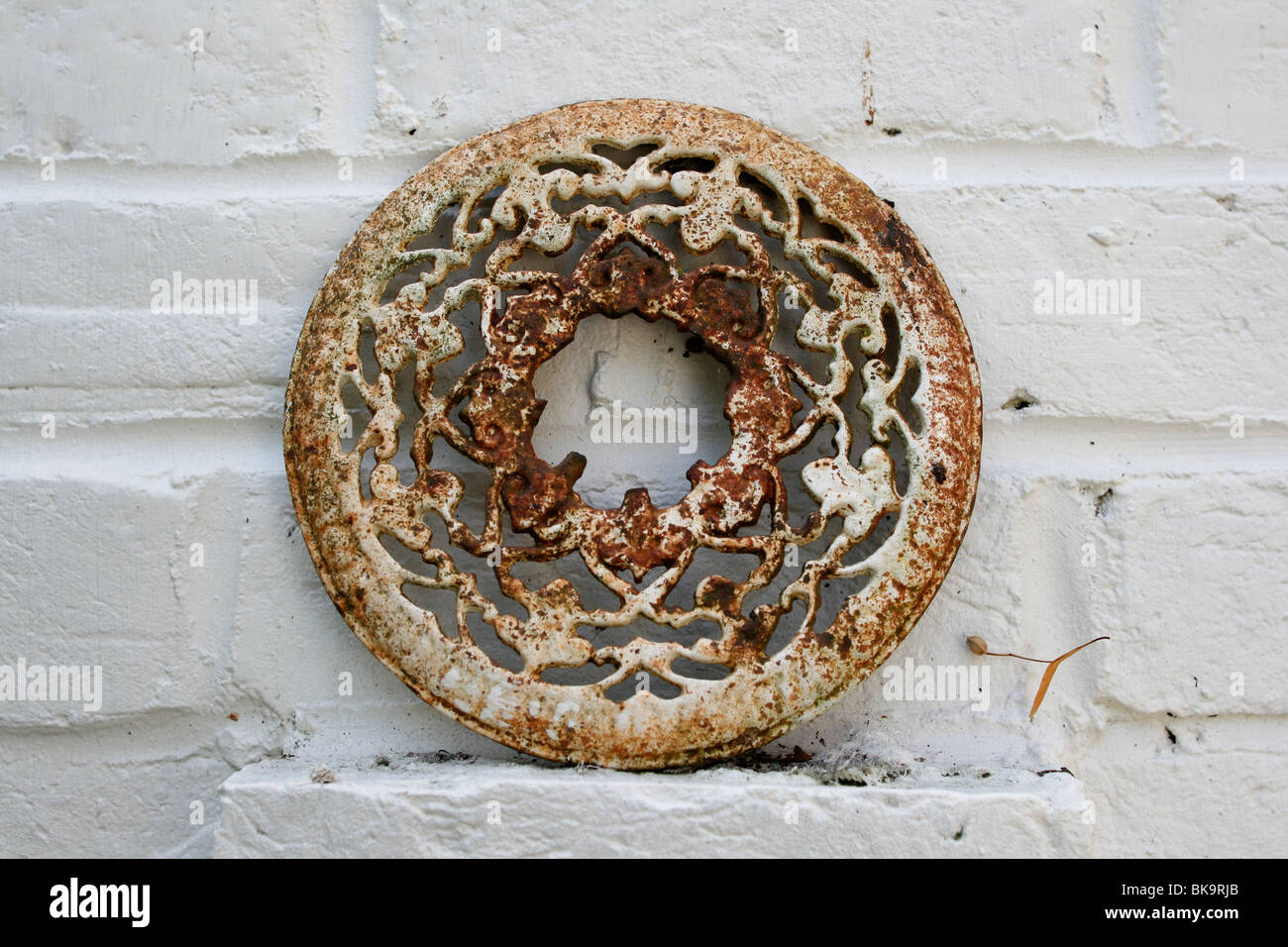 decorated metal plate hanging on a painted brick garden wall Stock