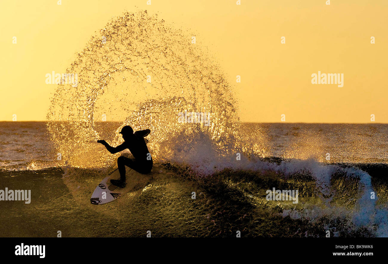 A surfer is silhouetted by the sun at Brims Ness, near Thurso, Scotland. The sun sets in the north of Scotland. Stock Photo