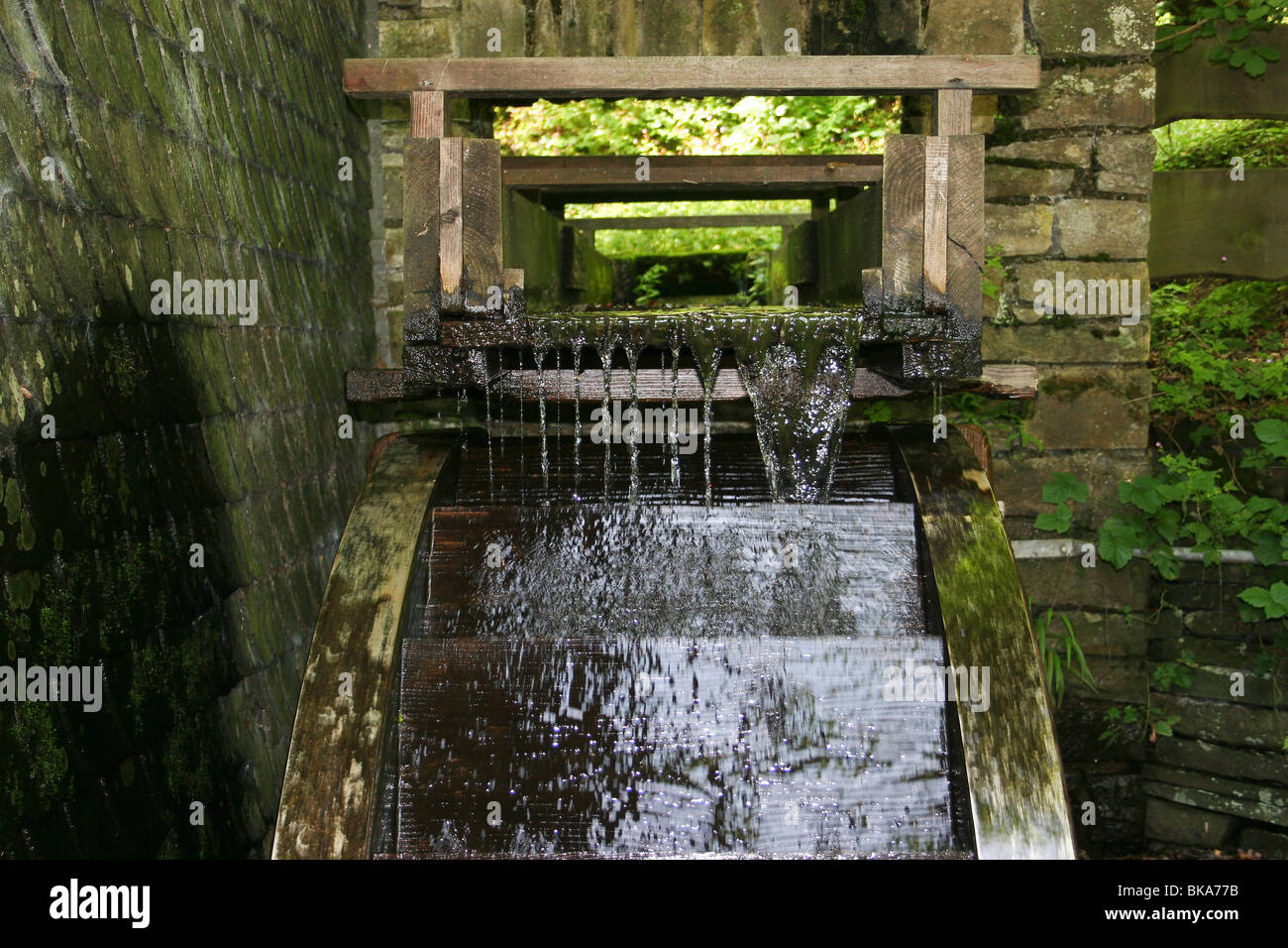 Water streaming through the flume towards an overshot water wheel Stock