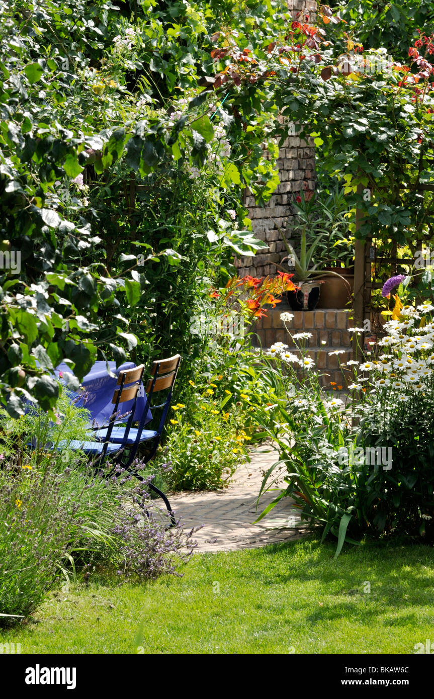 Seating area with rose arch in a backyard garden. Design: Jutta Wahren Stock Photo