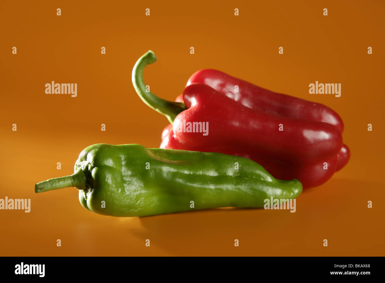 Red and green pepper over orange yellow background Stock Photo - Alamy