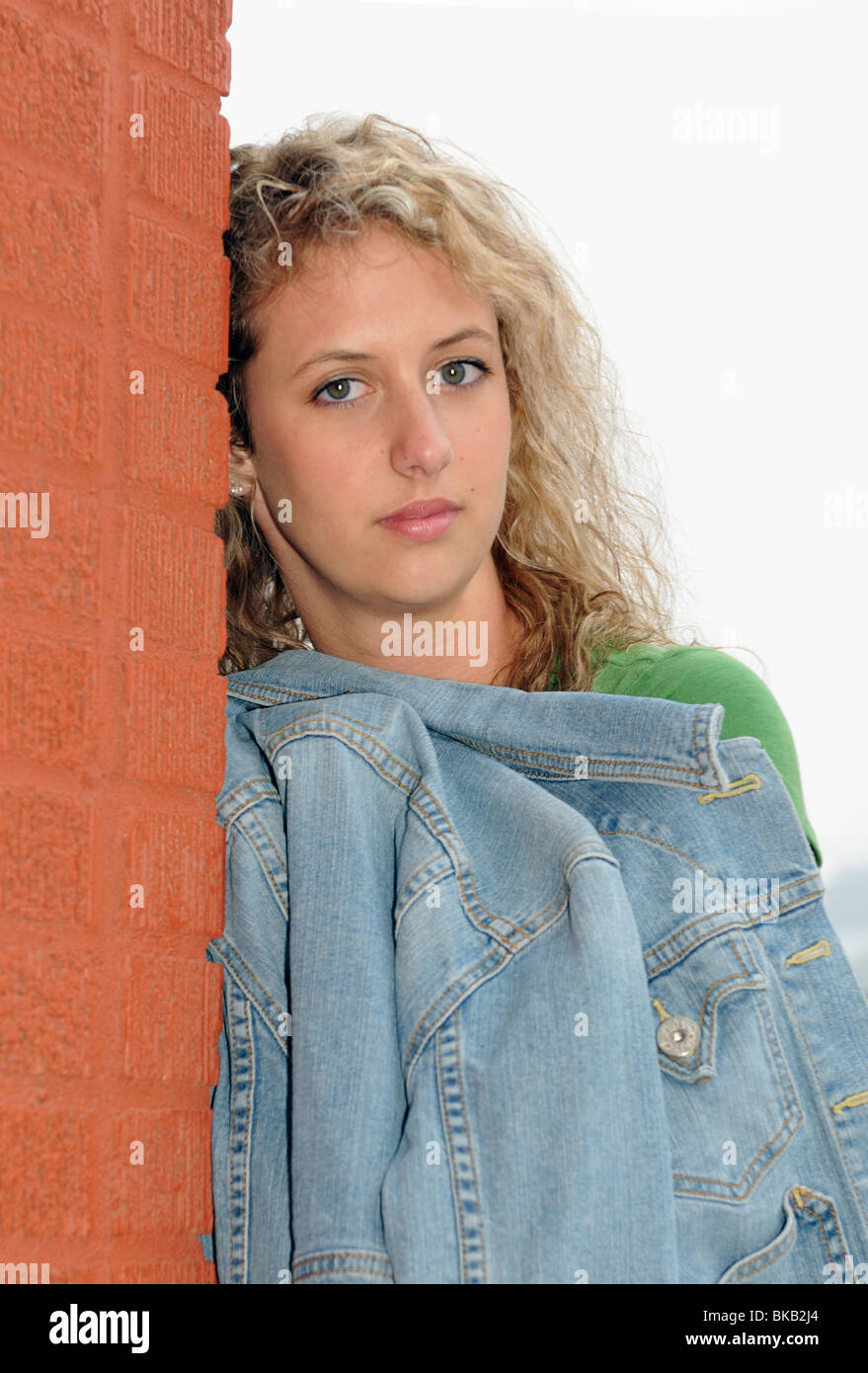 A sad caucasian teenage girl leans against a brick building. Stock Photo