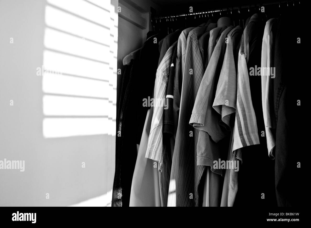Clothes hanging up in a wardrobe, with sunlit shadow from venetian blinds.  (B&W) Stock Photo