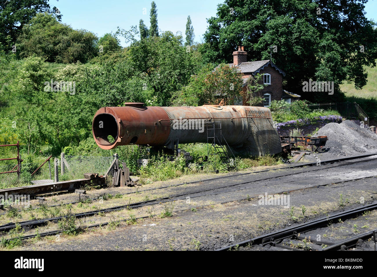 An old boiler removed from a steam locomotive waits to be repaired at the side of the railway tracks in the countryside Stock Photo