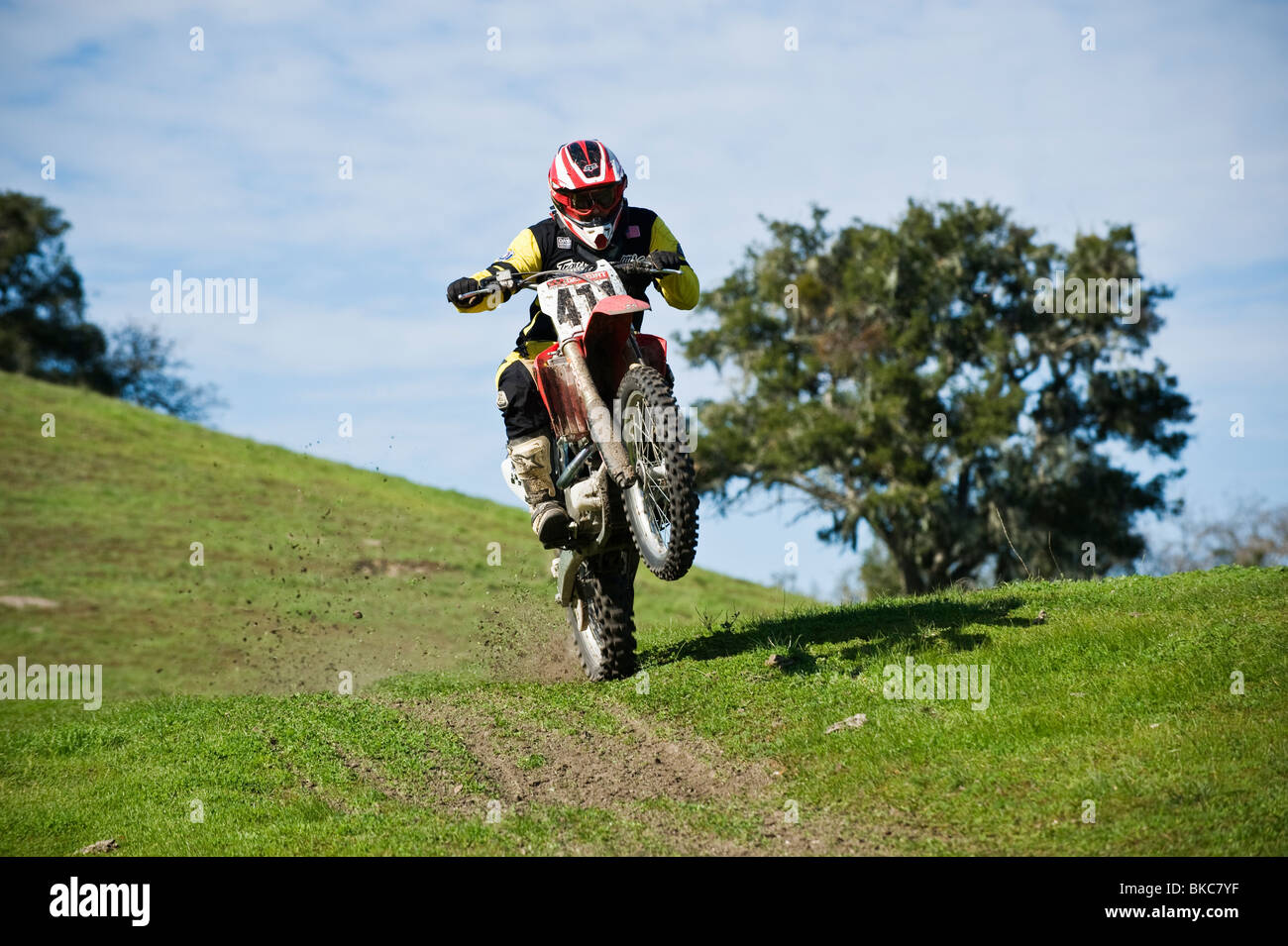 Adult male dirtbike rider wheelies motorycle on dirt trail, California Stock Photo