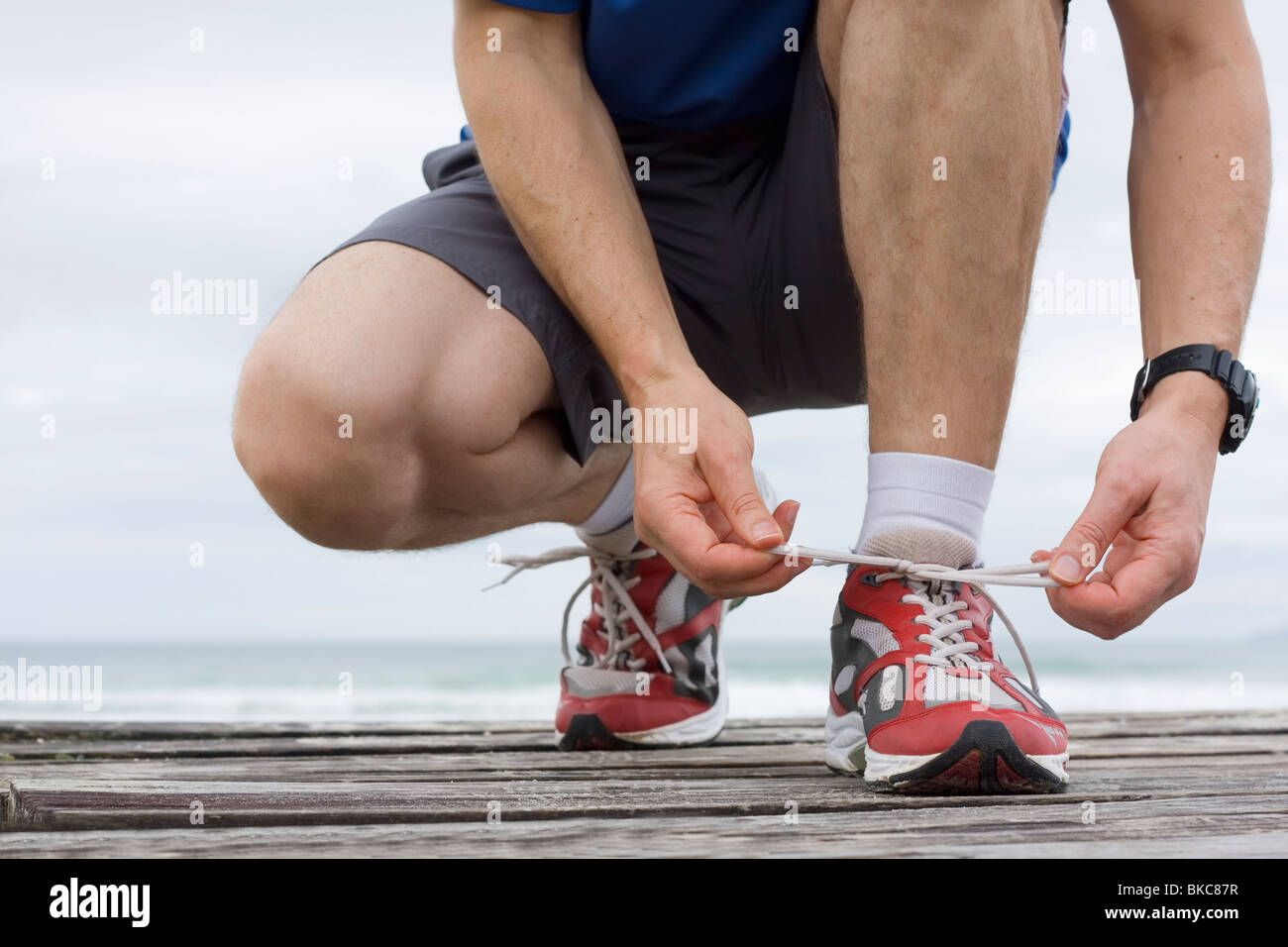 Runner tying shoelace in front of the sea Stock Photo