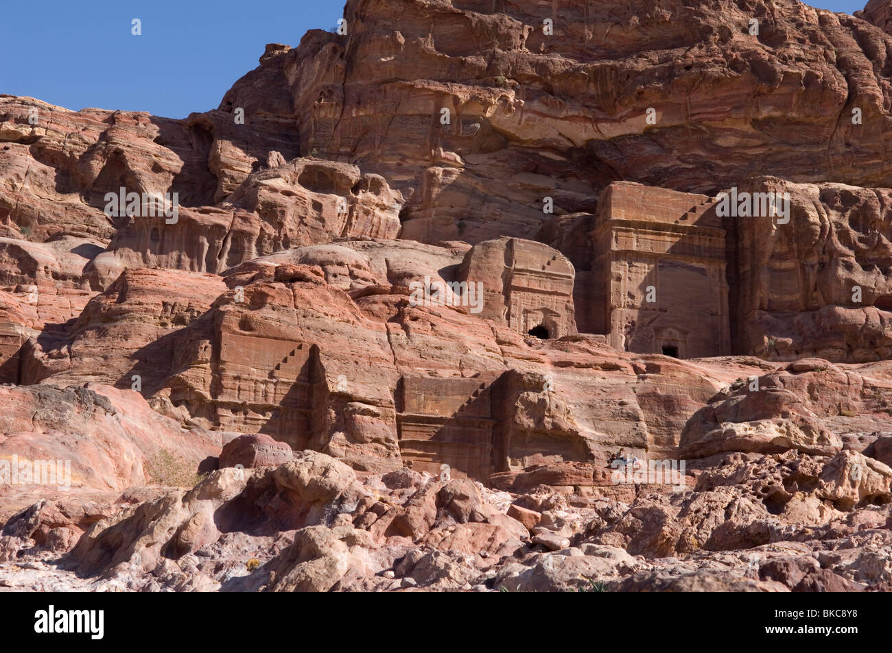 Small group of tourists sitting in front of a cluster of Nabataean tombs. Petra, Jordan Stock Photo