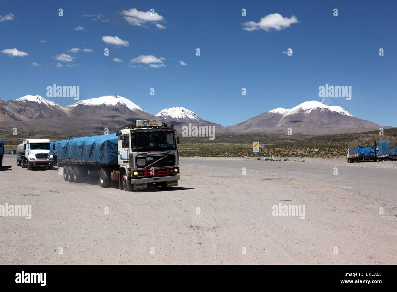 Trucks waiting at customs control on Chile side of international border at Chungara, snow capped volcanos in background, Bolivia / Chile border Stock Photo