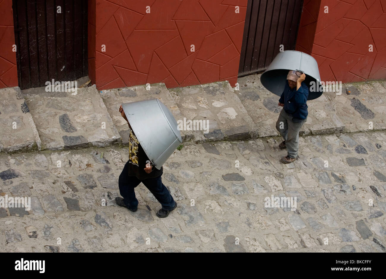 Men carry large metal pans for sale or barter in the Sunday market in Cuetzalan del Progreso, Mexico Stock Photo