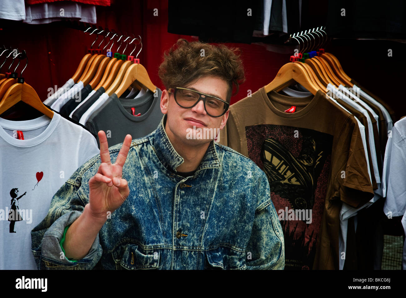 A young male adult wearing glasses at a clothing market stall owner at Camden Market North London UK Stock Photo