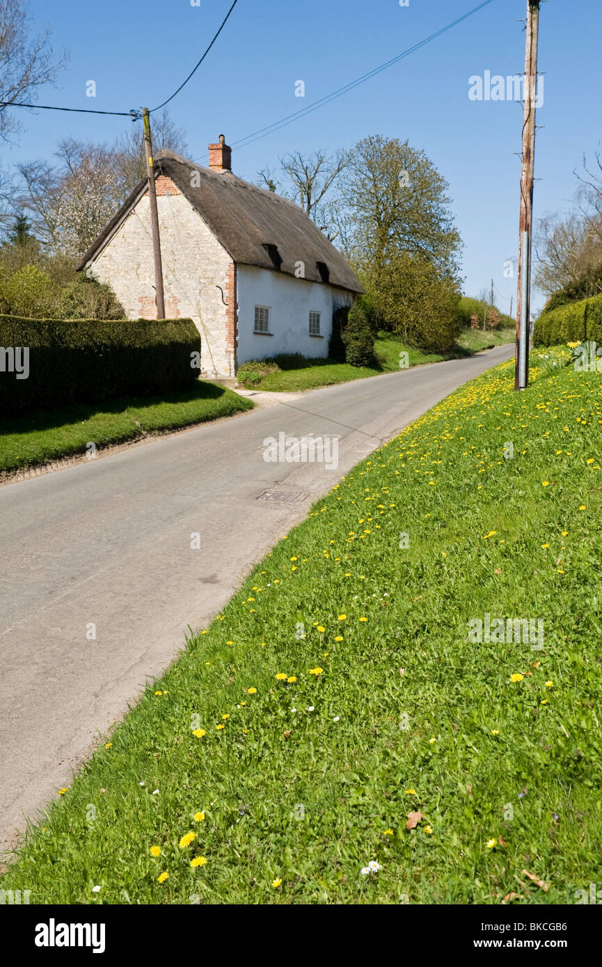 A quiet countryside road with a traditional thatched cottage on one side and a grass bank opposite in Chilton Oxfordshire Stock Photo