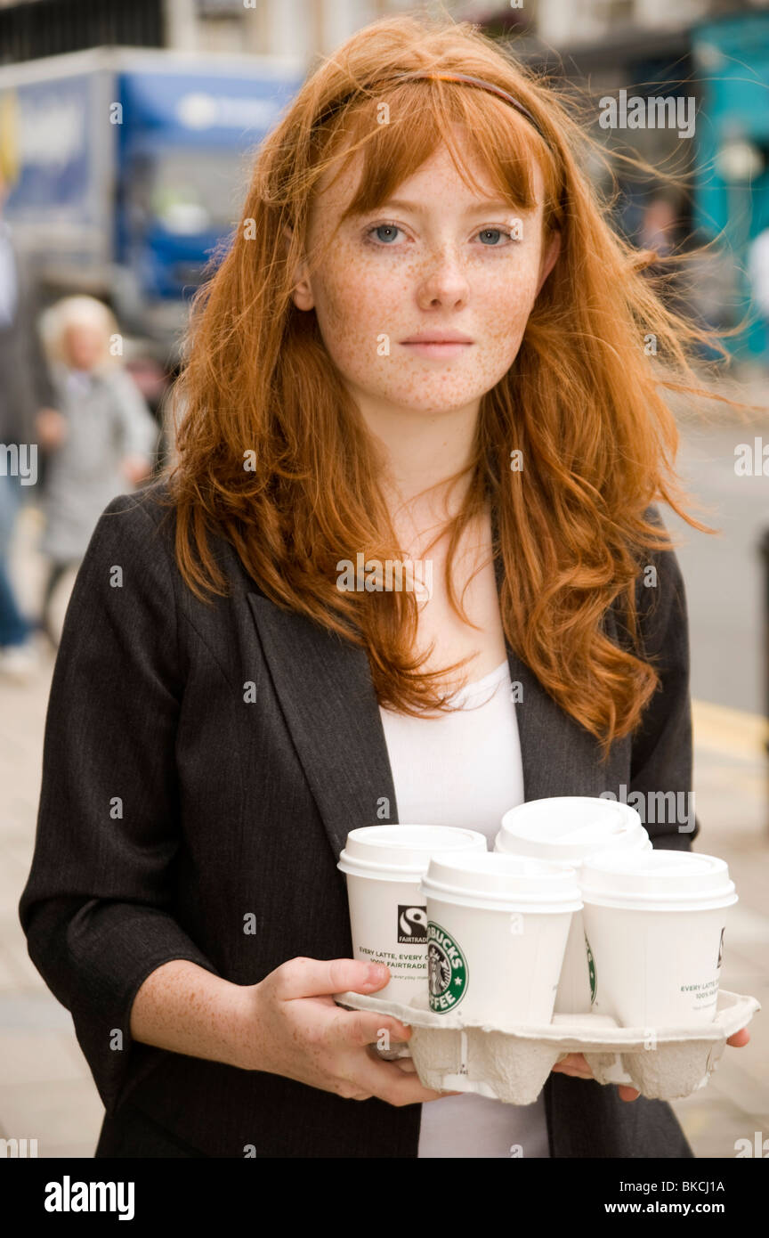 portrait of a teenage girl with red hair blue eyes and lots of freckles carrying a tray of Starbucks drinks Stock Photo