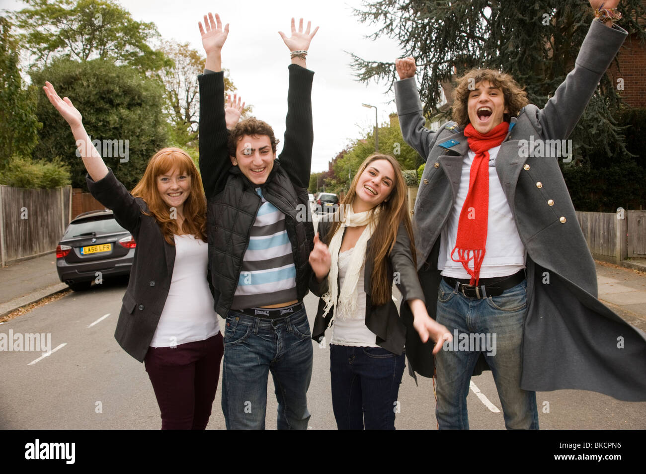 group of teenagers outside in the street leaping in the air as if they have finished school or exams and are celebrating Stock Photo