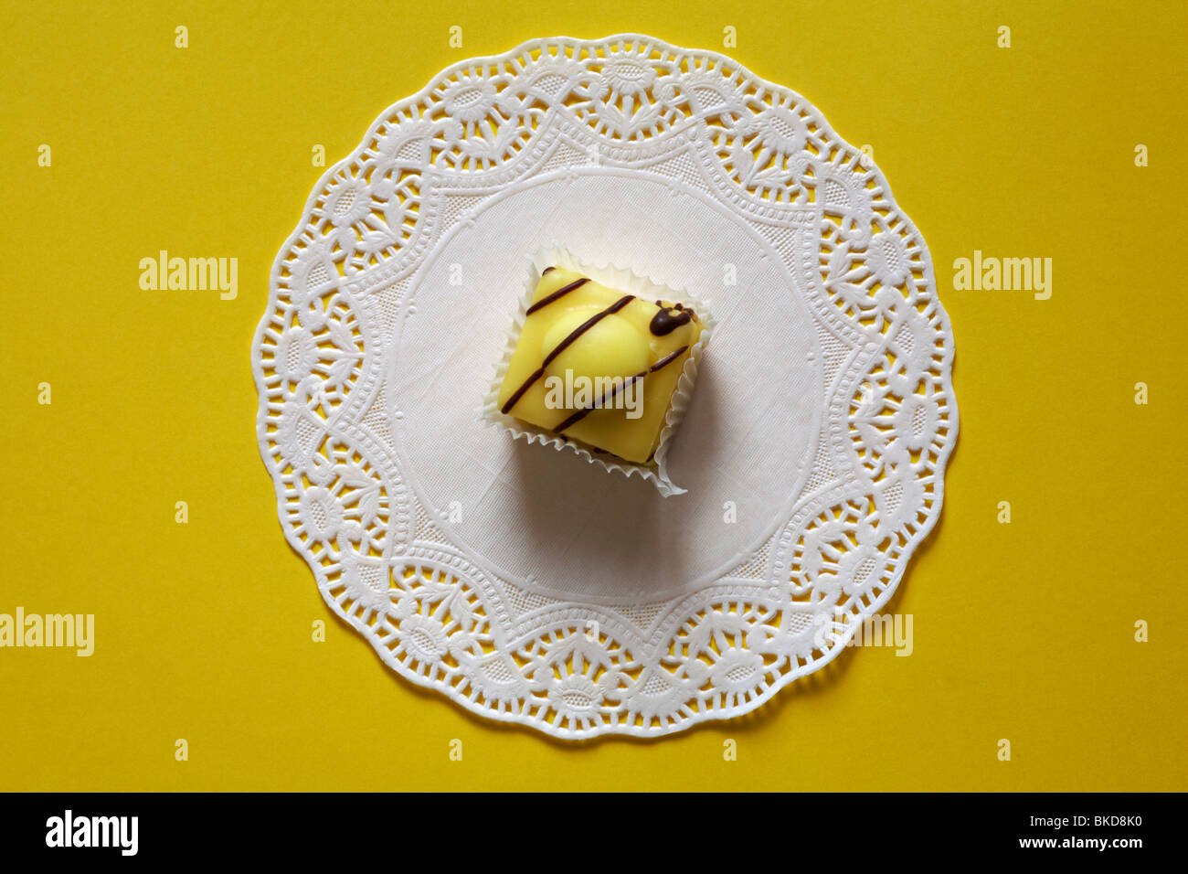 Special Edition Lemon French Fancies by Mr Kipling on white doily set on yellow background Stock Photo