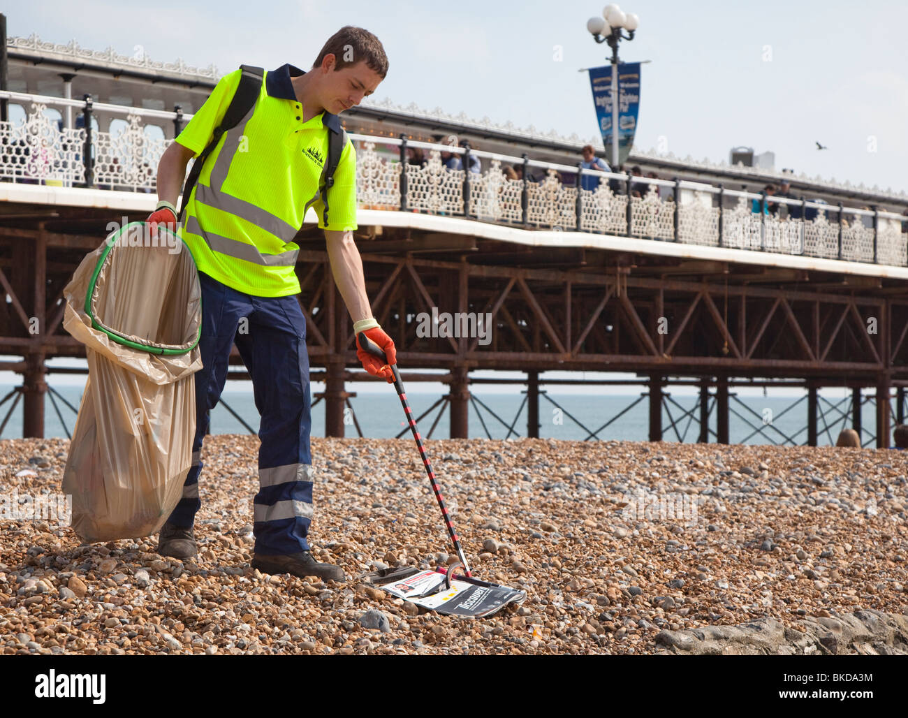 Council workman picking up litter on beach beneath Brighton pier England UK Stock Photo