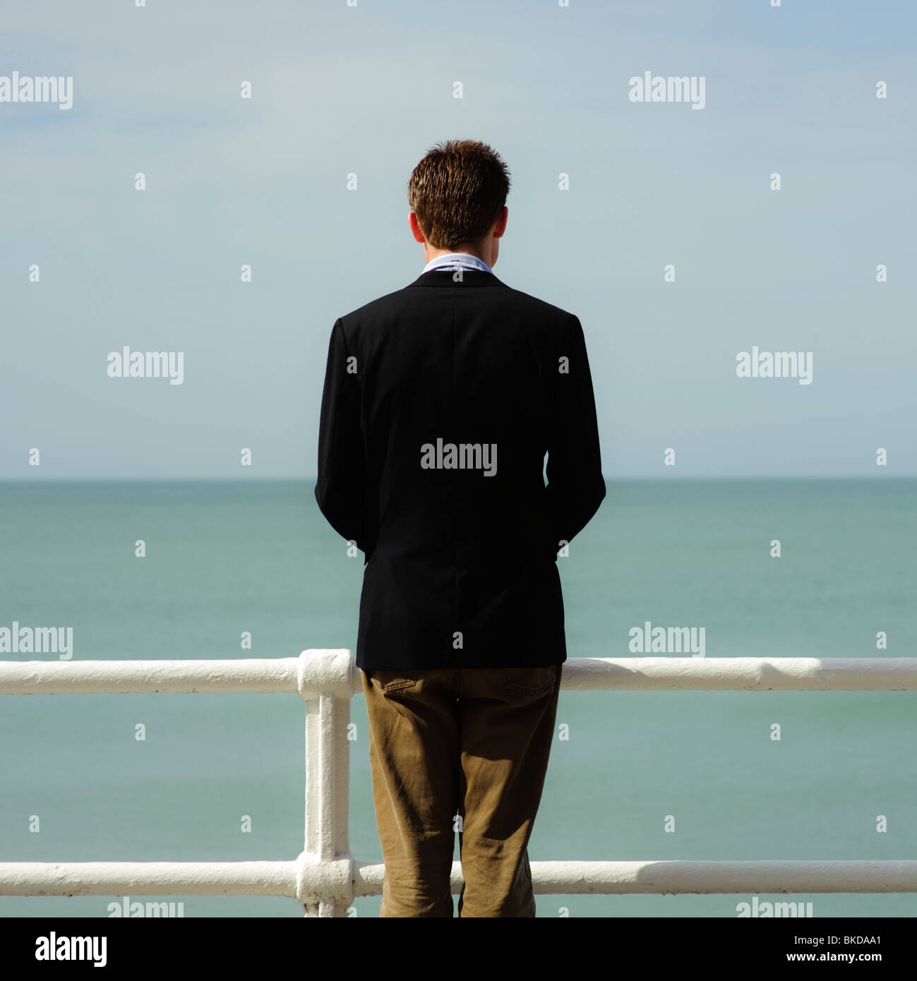 rear view of a single man , facing away, standing alone looking out to sea on a summer day Stock Photo