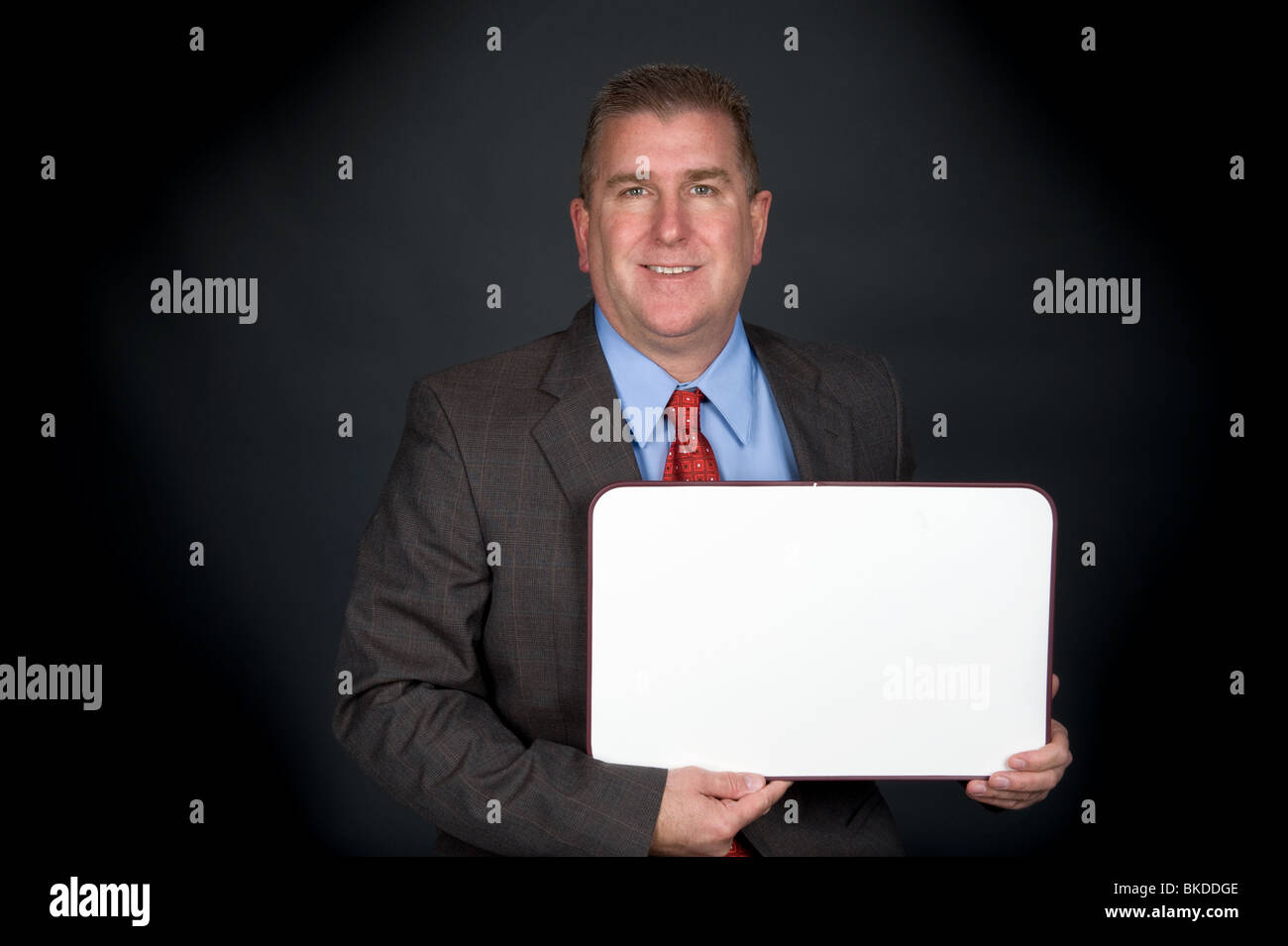 A well dressed professional businessman holds a blank whiteboard. Board is left blank for designers to place copy. Stock Photo