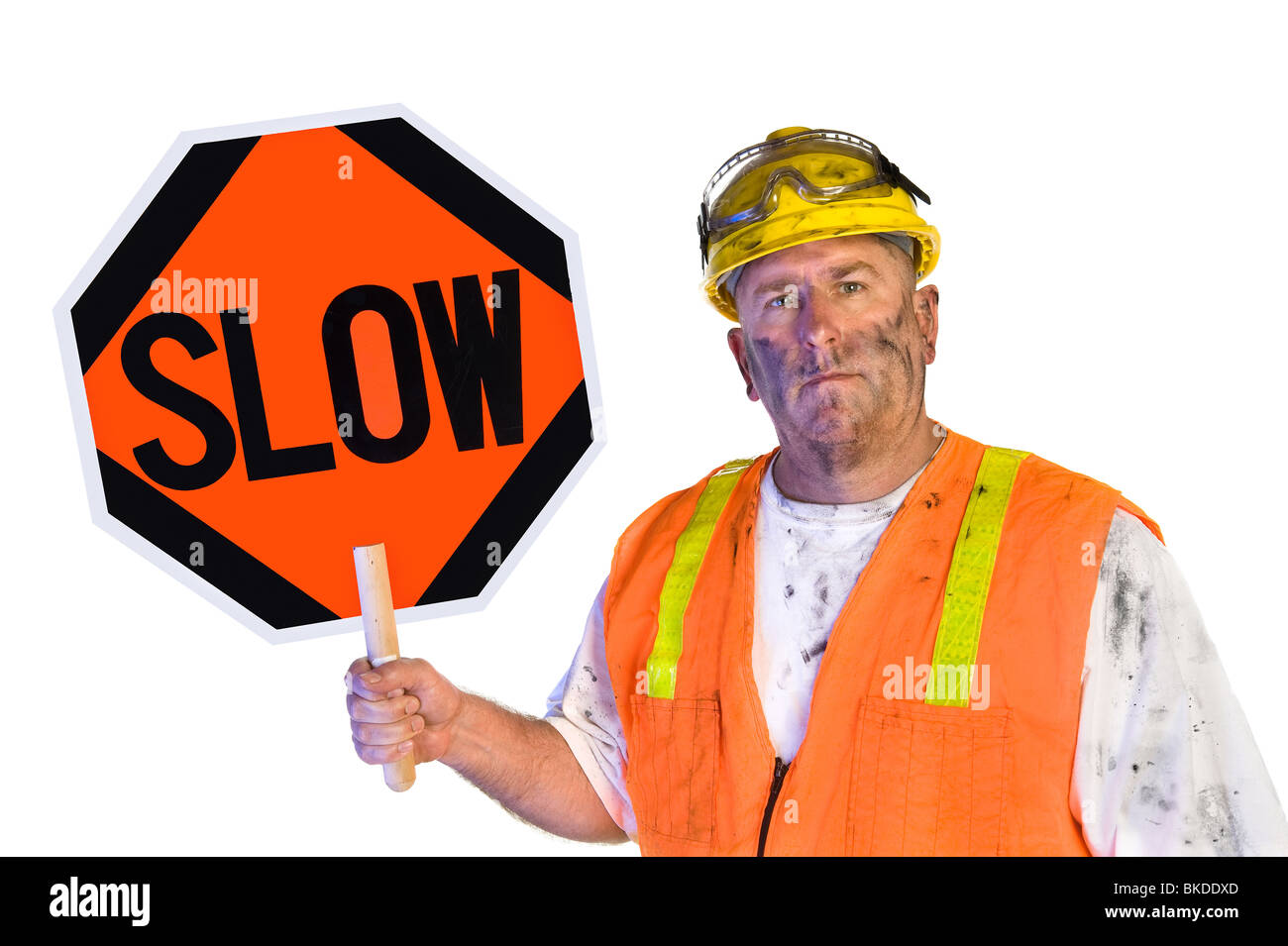 A dirty, grungy, greasy utility construction worker with hard hat, orange vest and eye protection holds up a slow sign. Stock Photo