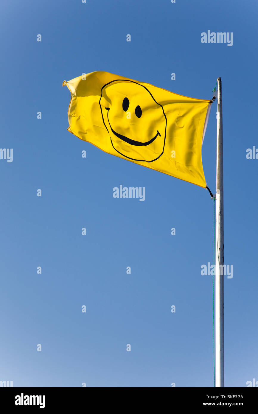 Yellow smiley face flag against a clear blue sky. Stock Photo