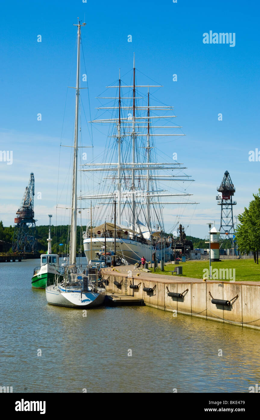 The Aura River flowing through Turku, Finland, with the historic tall ship Suomen Joutsen docked prominently on the left, and colorful buildings lining the opposite bank.